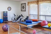 Well-equipped interior therapy room with mats, balls, bikes, and a large window.