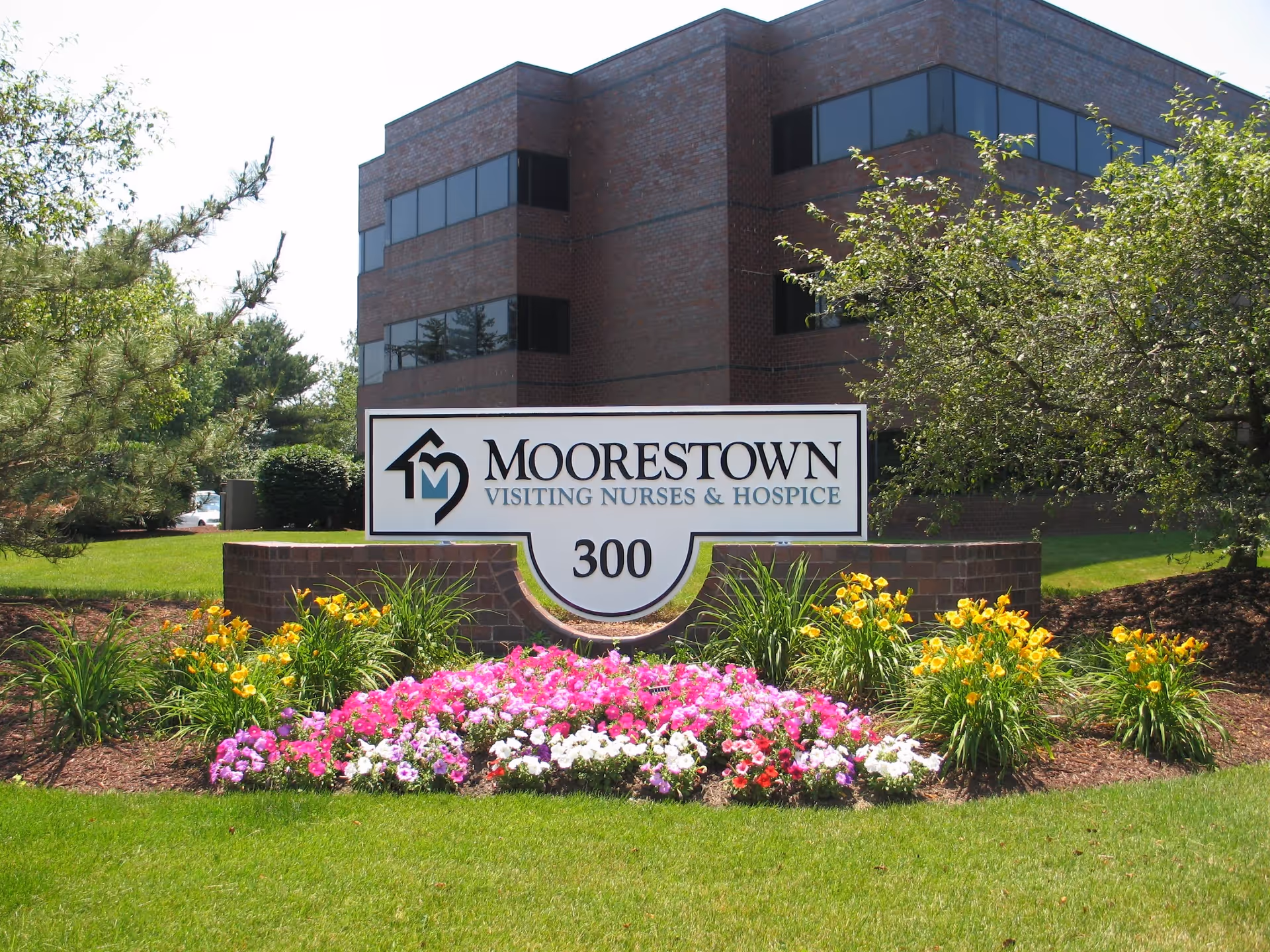 Front exterior of Moorestown Visiting Nurses & Hospice building with a landscaped sign and flowers.