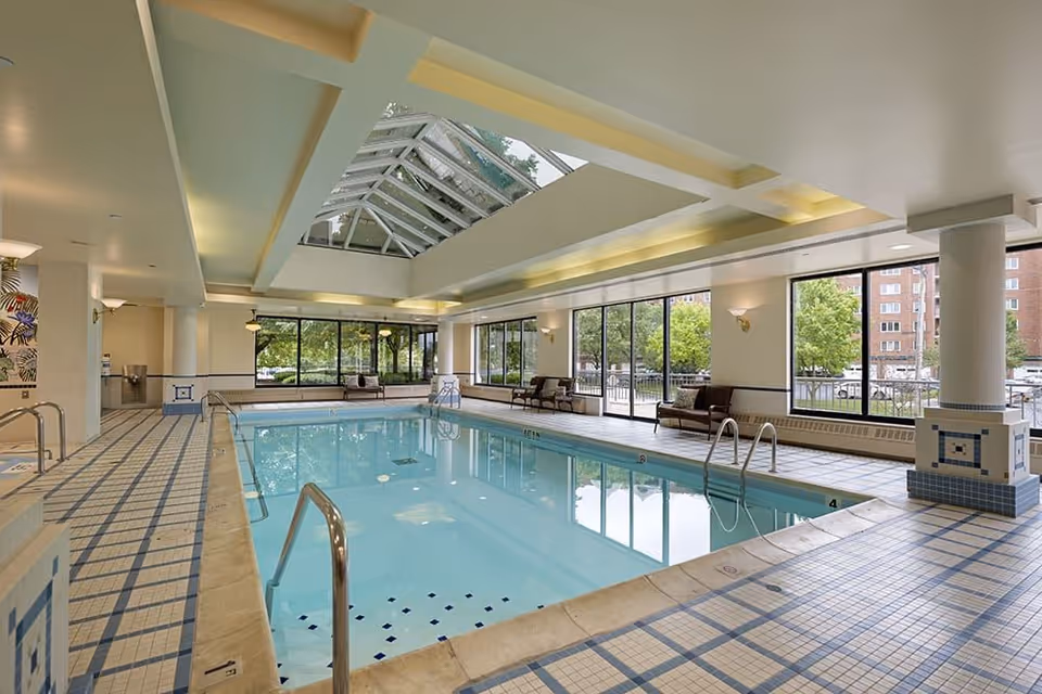 Bright indoor swimming pool with a skylight, large windows, tiled deck and seating along the sides.
