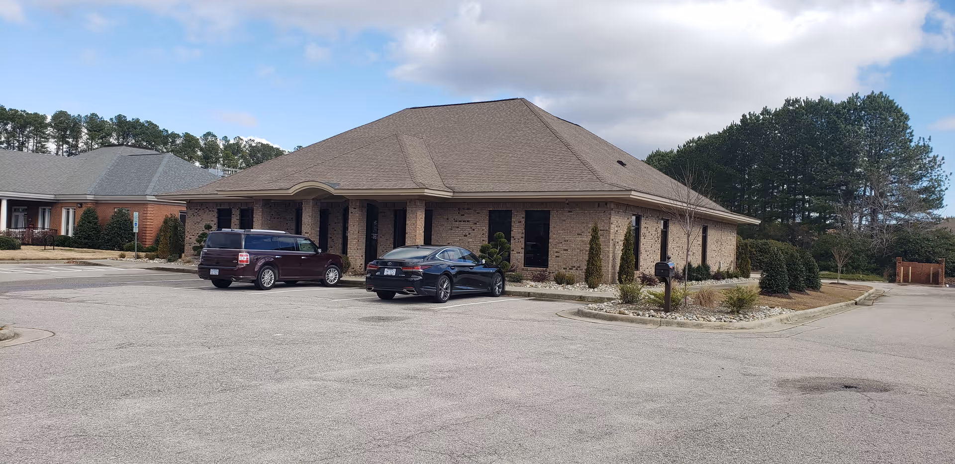 Single-story brick facility with a curved entrance and cars parked in front.