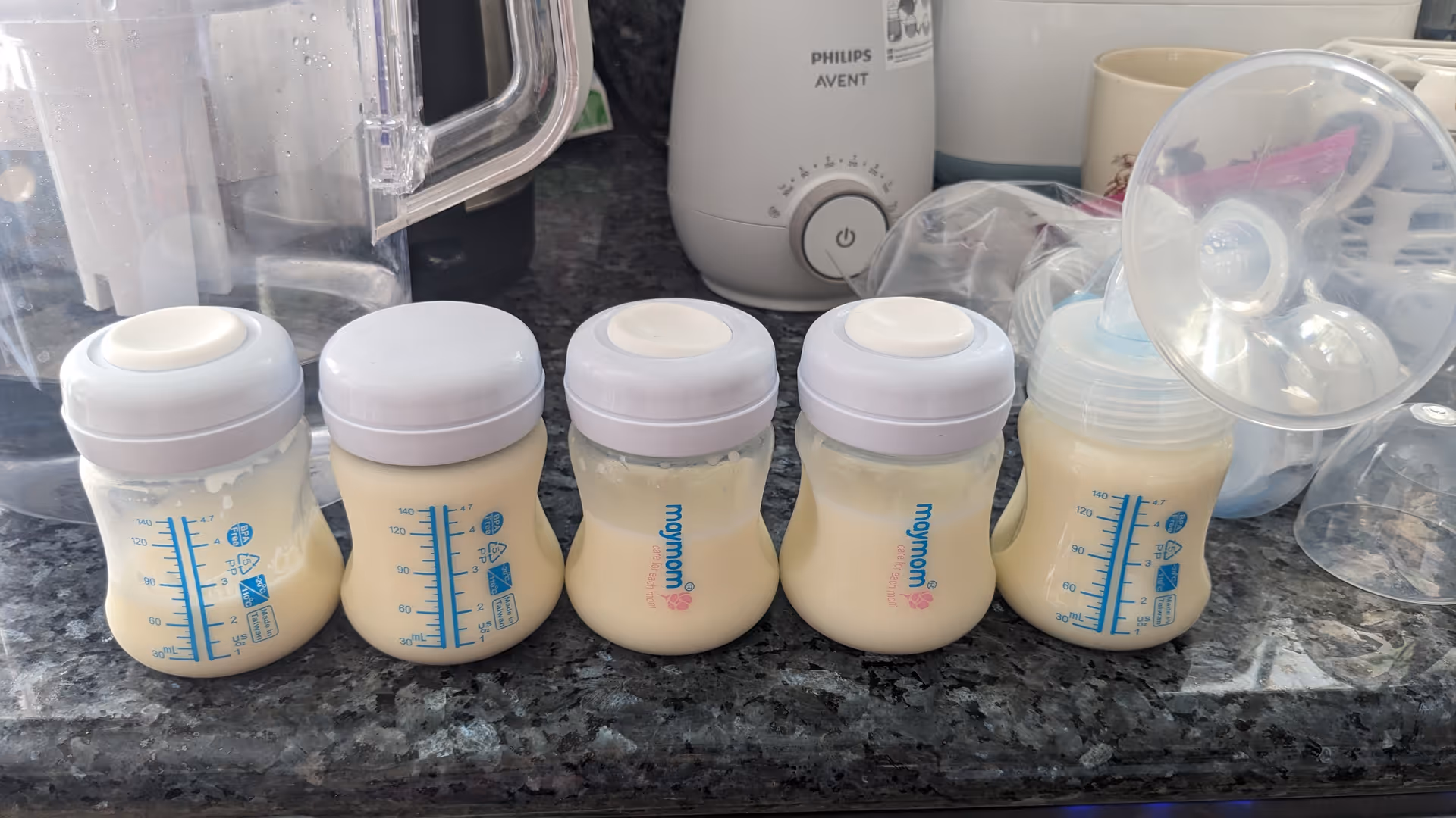 Row of baby bottles filled with milk lined up on a kitchen counter with appliances.