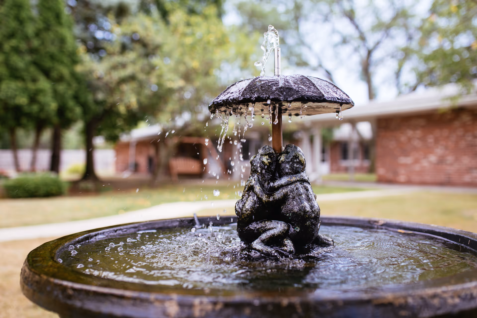 Outdoor fountain statue with umbrella centerpiece in a brick senior living courtyard