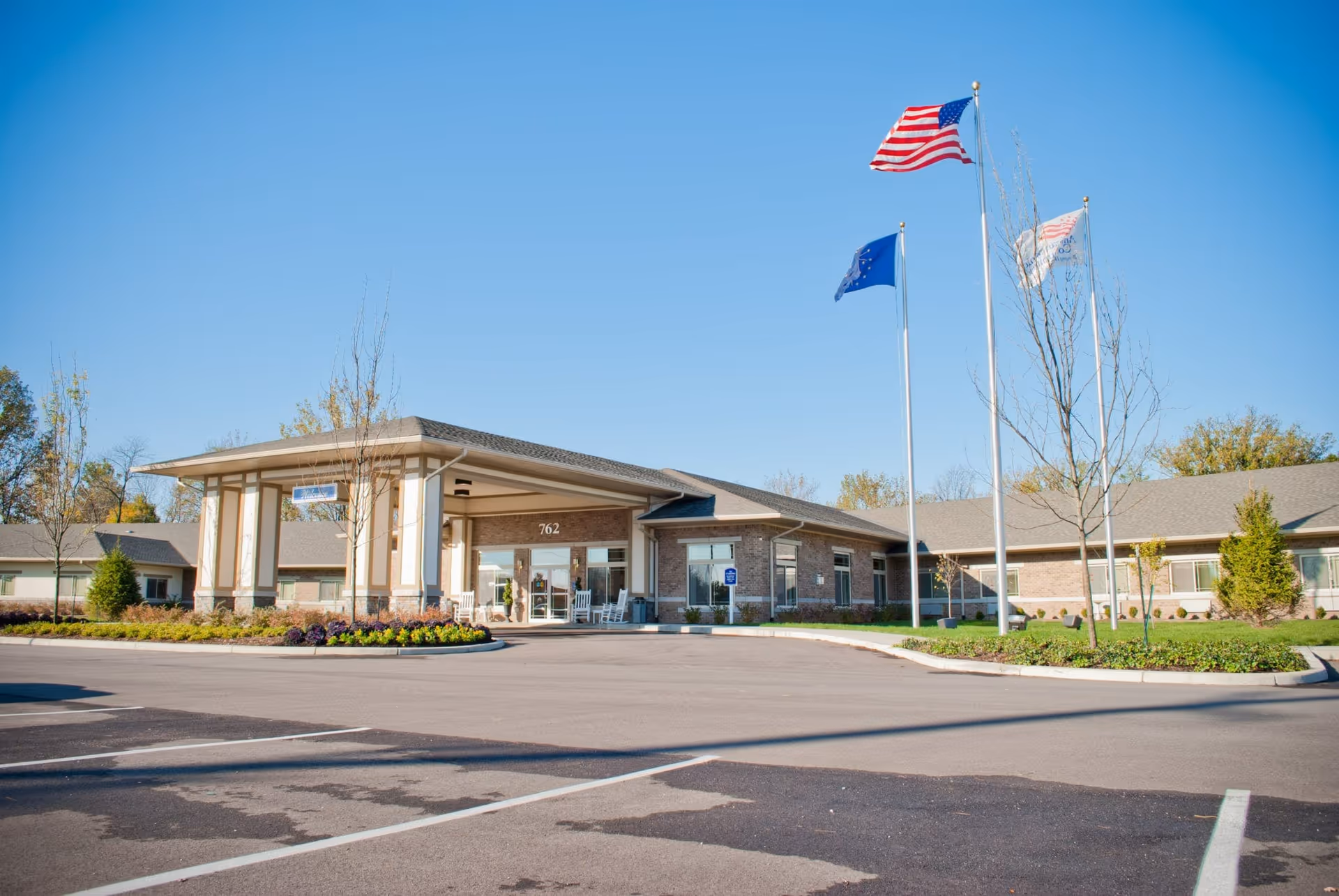 Exterior view of Countryside Meadows facility showing a single-story building with a covered entrance, three flagpoles with American, state, and facility flags, and a parking lot in front under a clear blue sky.