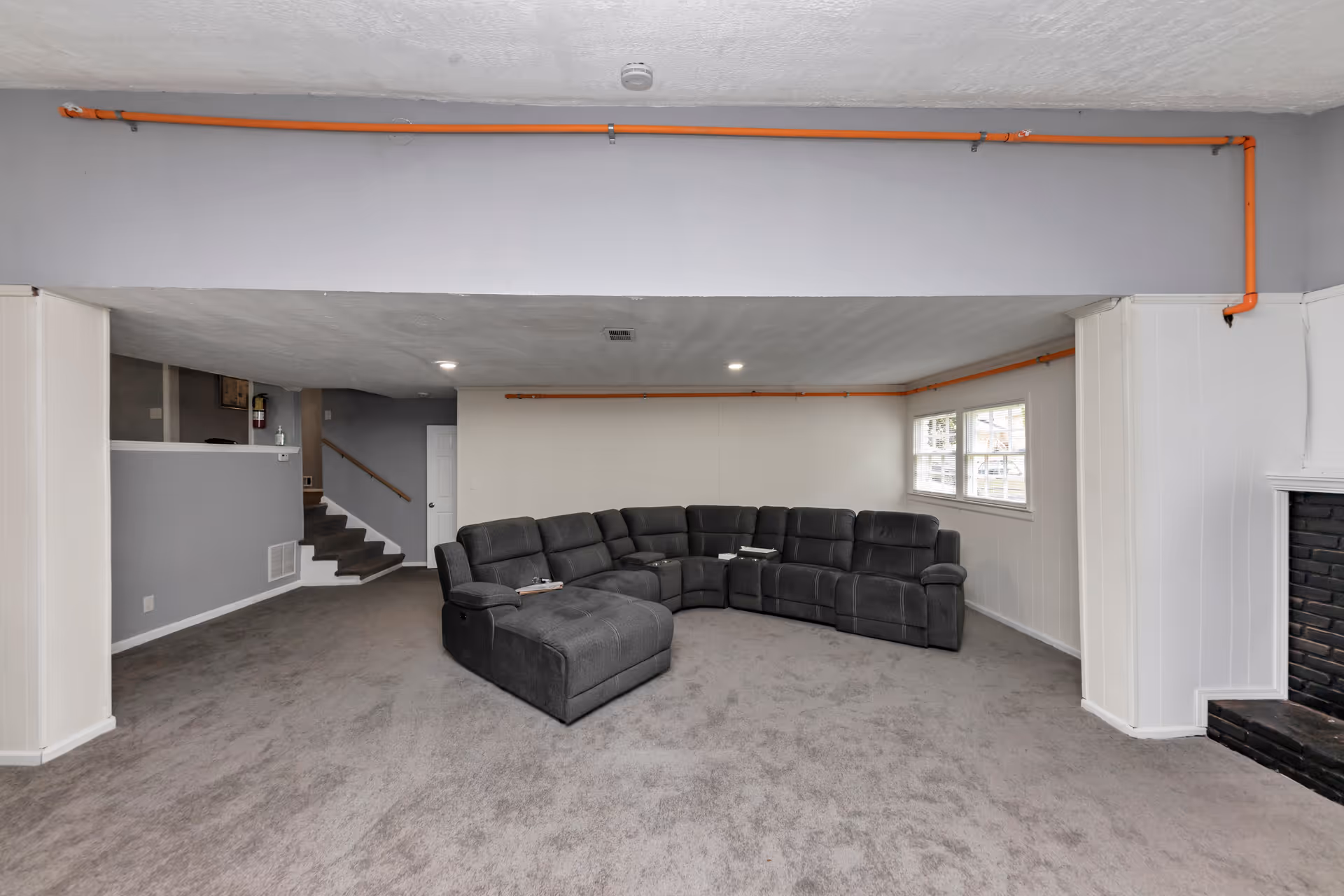Basement-style living room with gray sectional sofa, carpet, stairs, and a fireplace.