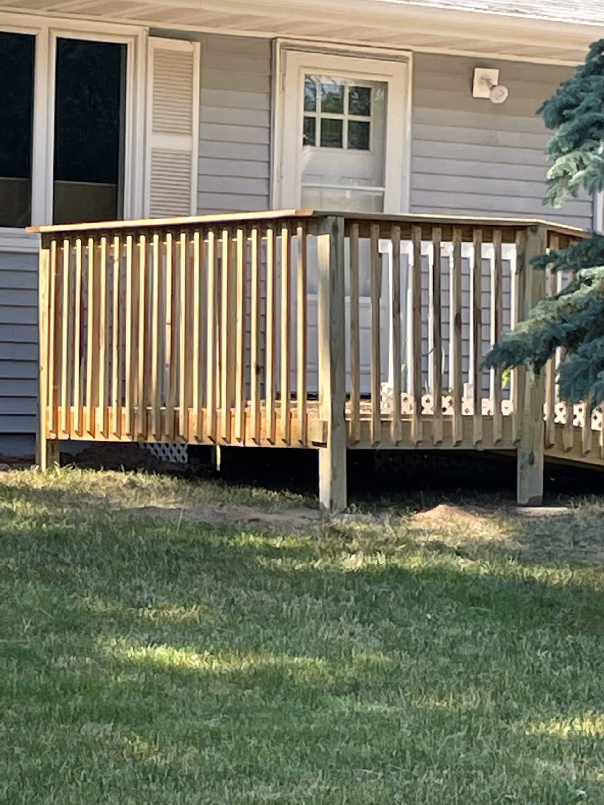 A wooden deck with railing attaches to a gray residential home exterior; the yard is visible.