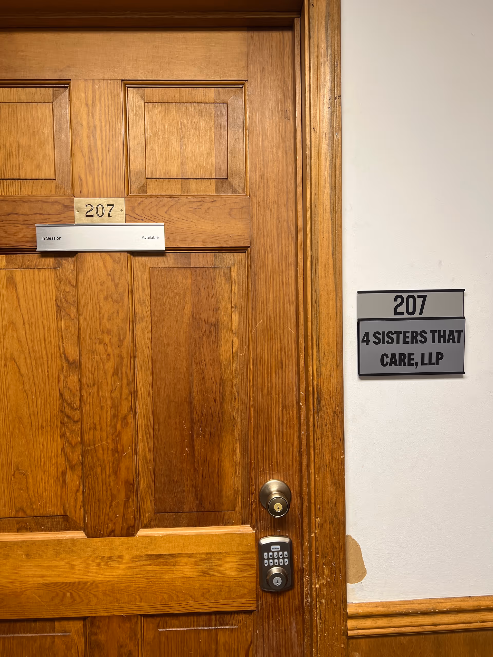 A wooden interior door labeled 207 with a wall plaque reading '4 Sisters That Care, LLP'