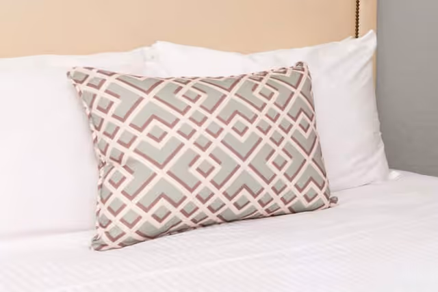Close-up of a neatly made bed with a geometric patterned decorative pillow.