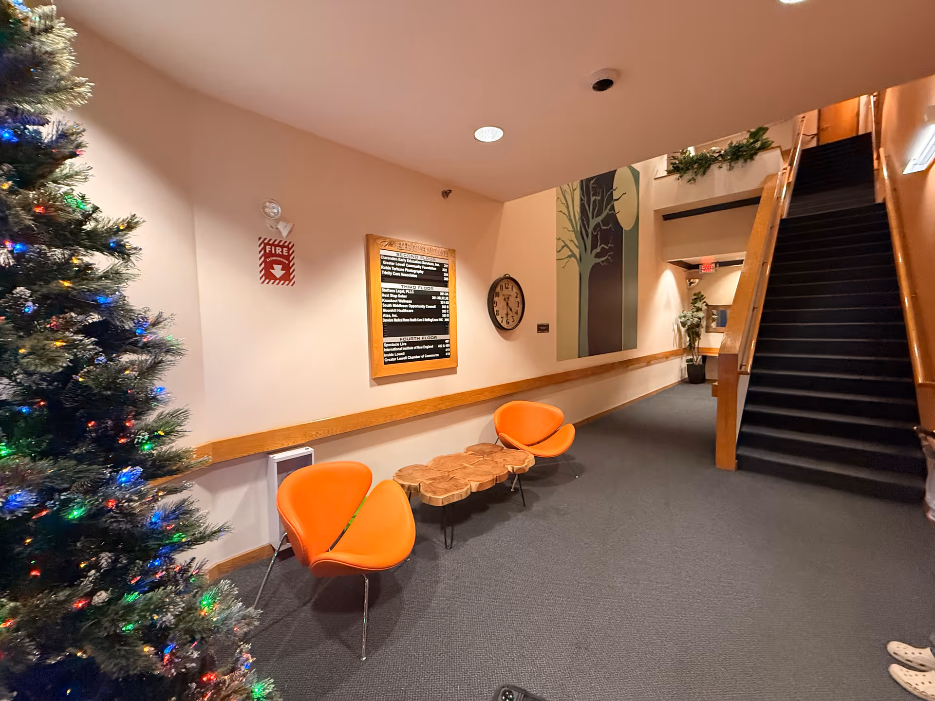 A hallway inside a senior living facility with orange chairs, a Christmas tree, and stairs.