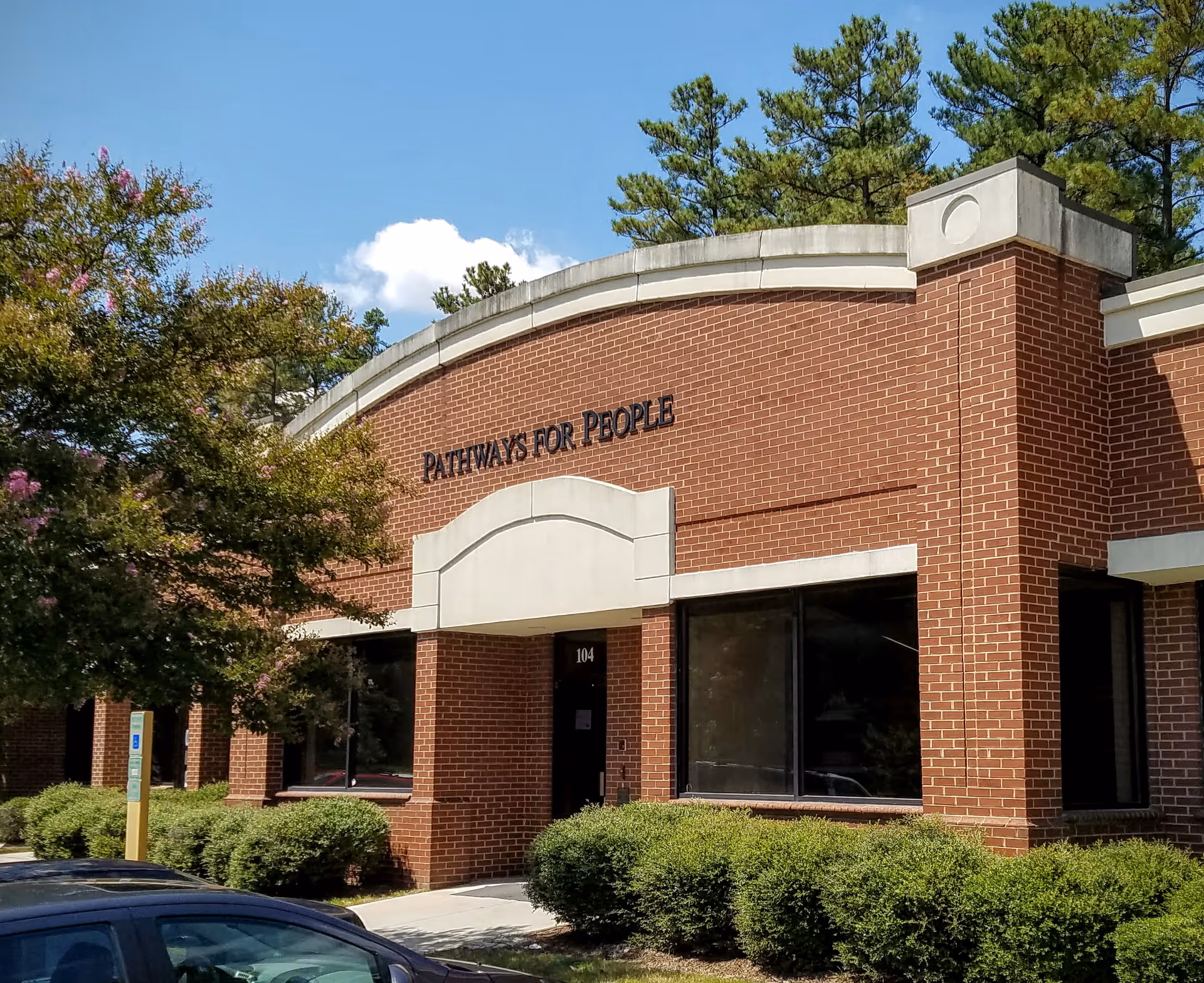 Brick building exterior with Pathways for People sign and manicured shrubs.
