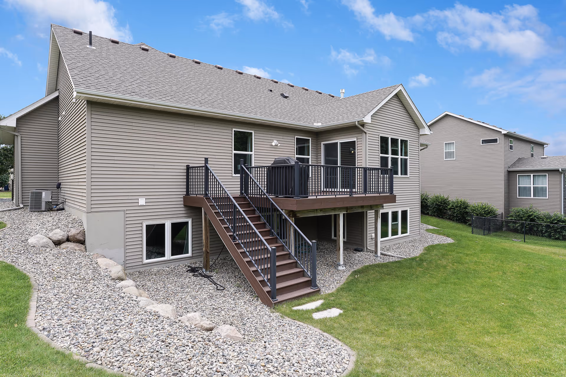 Two-story beige assisted-living building exterior with a wooden deck and green lawn.