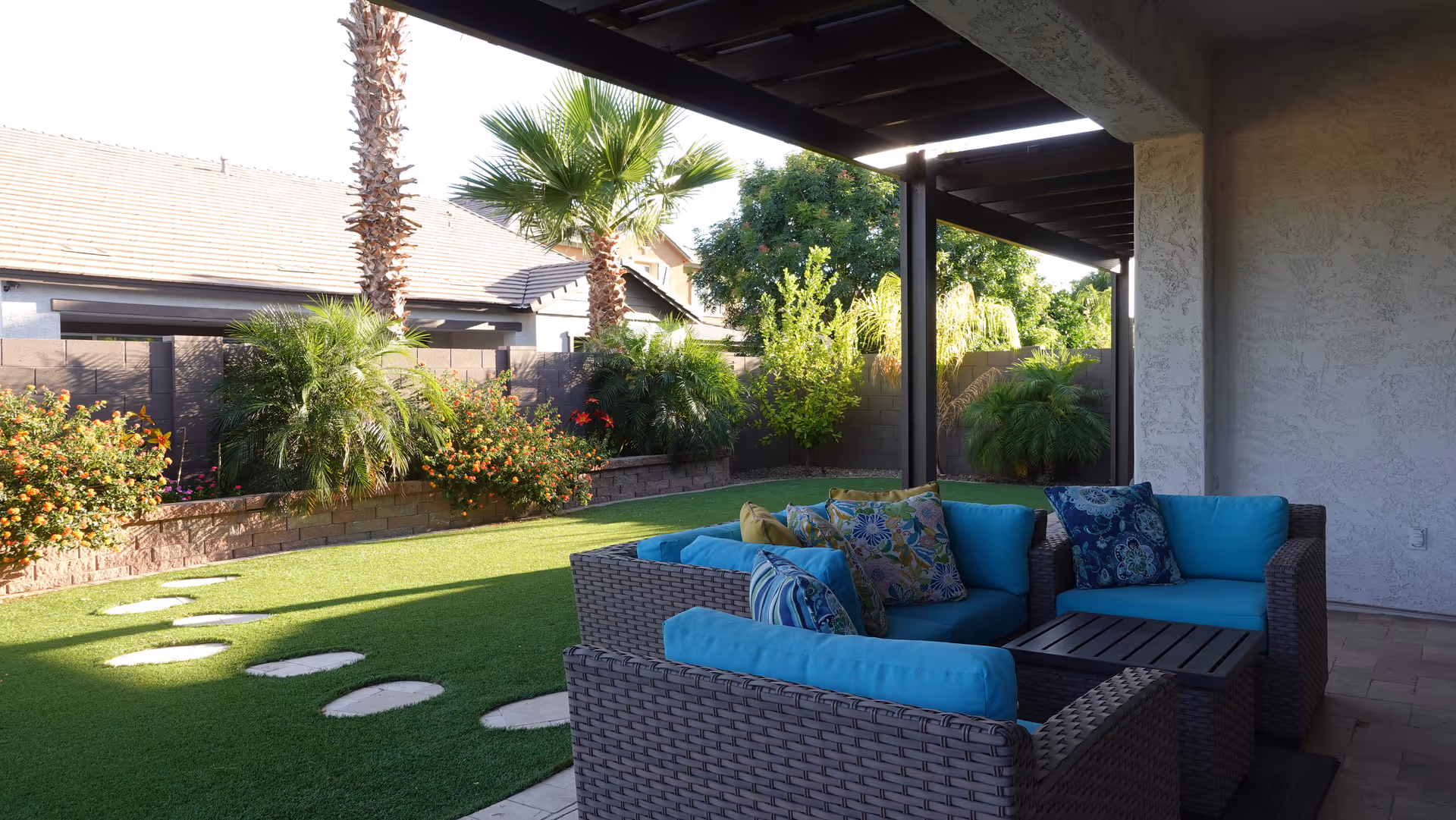 Covered outdoor patio with blue-cushioned wicker seating and tropical plants.
