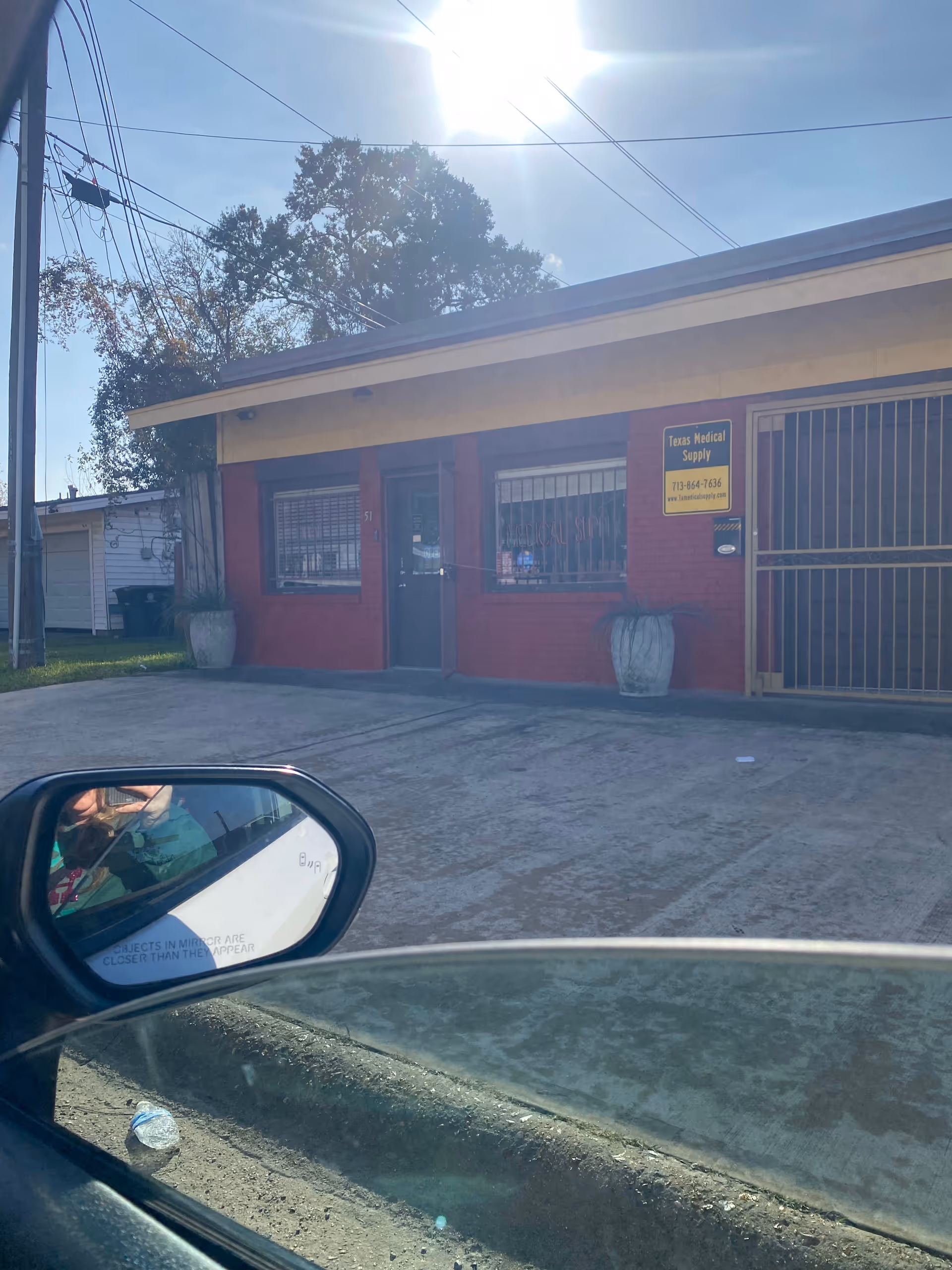 Exterior view of a red-brick Texas Medical Supply storefront with barred windows and driveway.