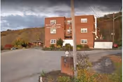 Brick nursing and rehabilitation center building with parking lot and surrounding trees.