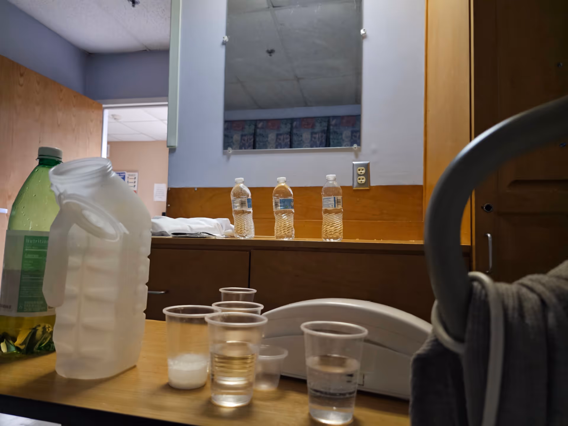 Counter with water bottles, cups, and a large jug in a small kitchen area.