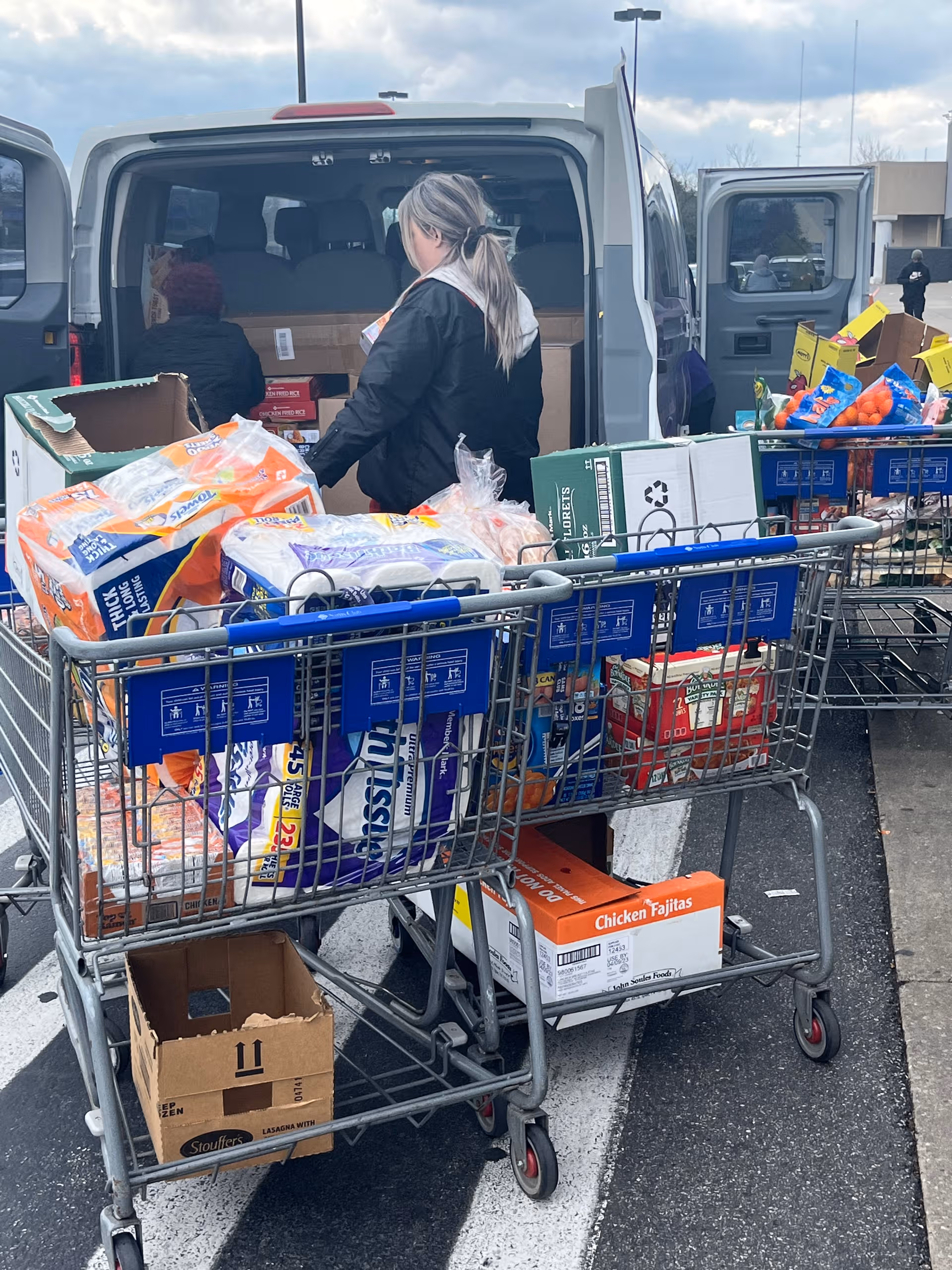 Volunteer loads groceries from a van into carts outside Faith, Hope and Charity senior living facility.