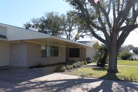 Exterior view of a single-story senior living facility entrance with trees.