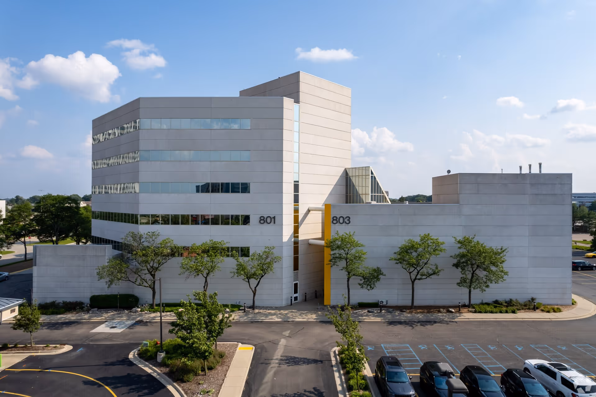 A modern white multi-wing building exterior with a parking lot and trees.