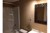 Bathroom interior with bathtub/shower combo, toilet, sink, and decorative mirror.