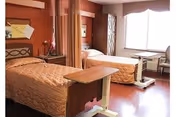 Two single beds in a shared care bedroom with bedside tables and curtains.