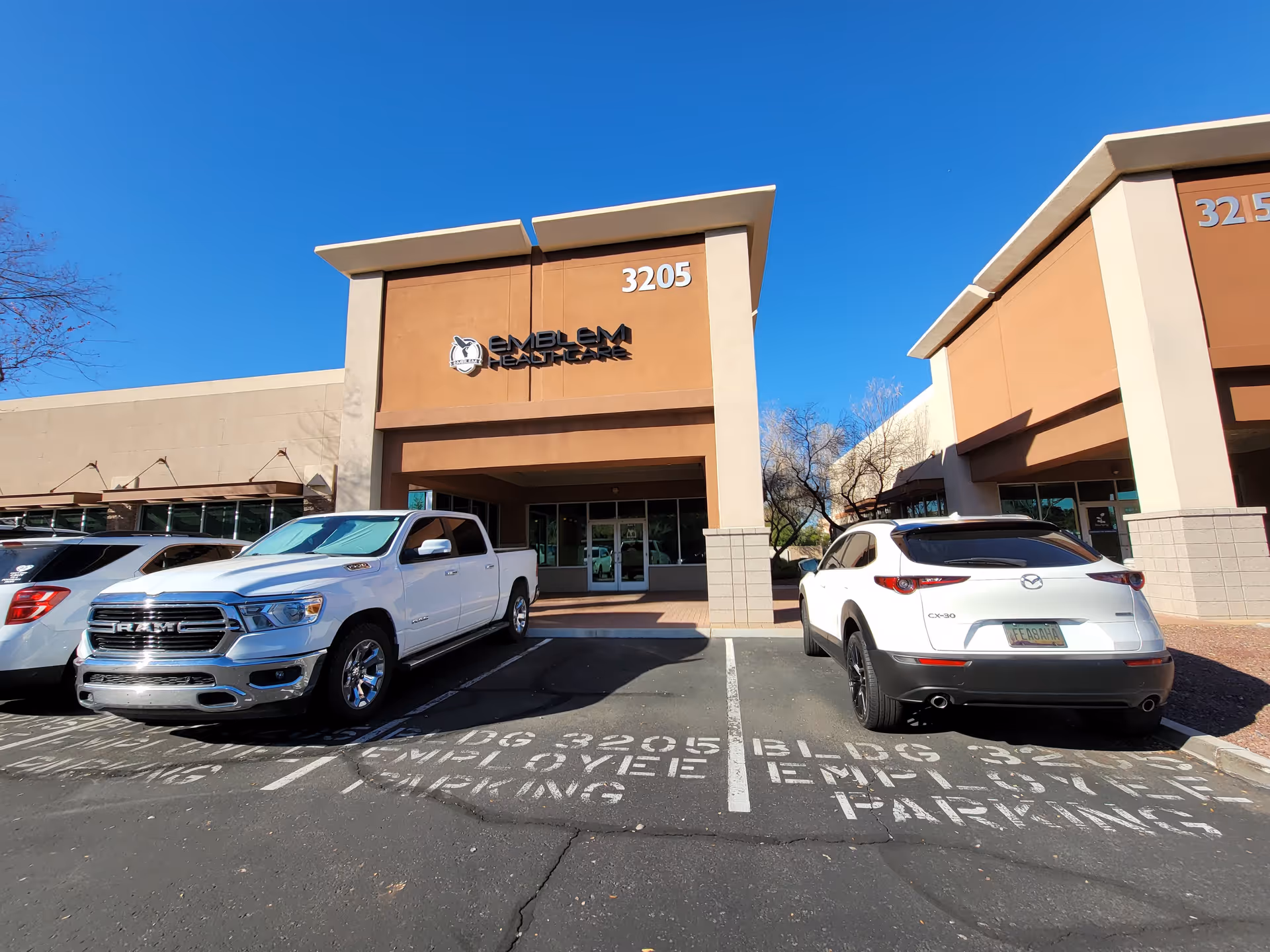 Senior living facility entrance with Emblem Healthcare signage, parked cars, and tan facade