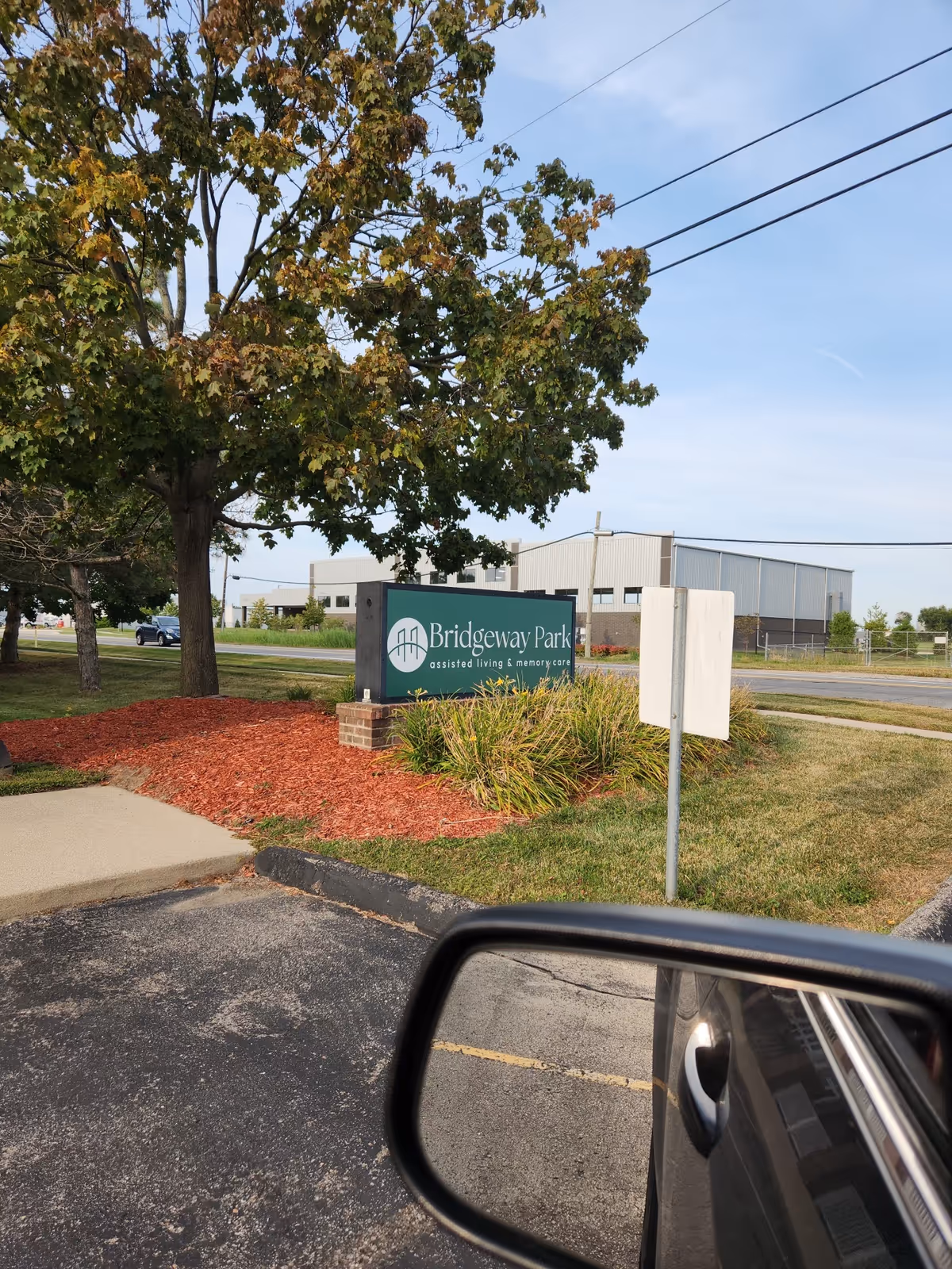 Outdoor view of a Bridgeway Park assisted living sign at the facility entrance with trees.