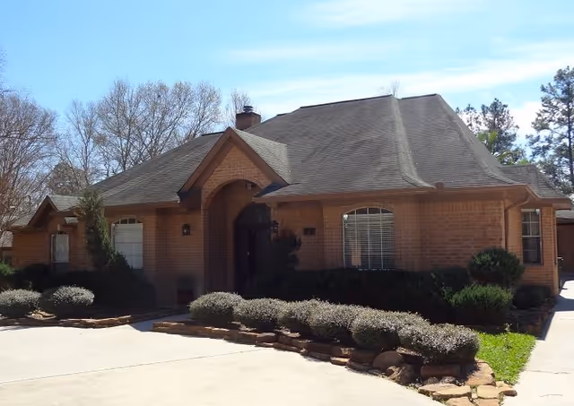 Brick senior living facility entrance with landscaped shrubs and a paved driveway.