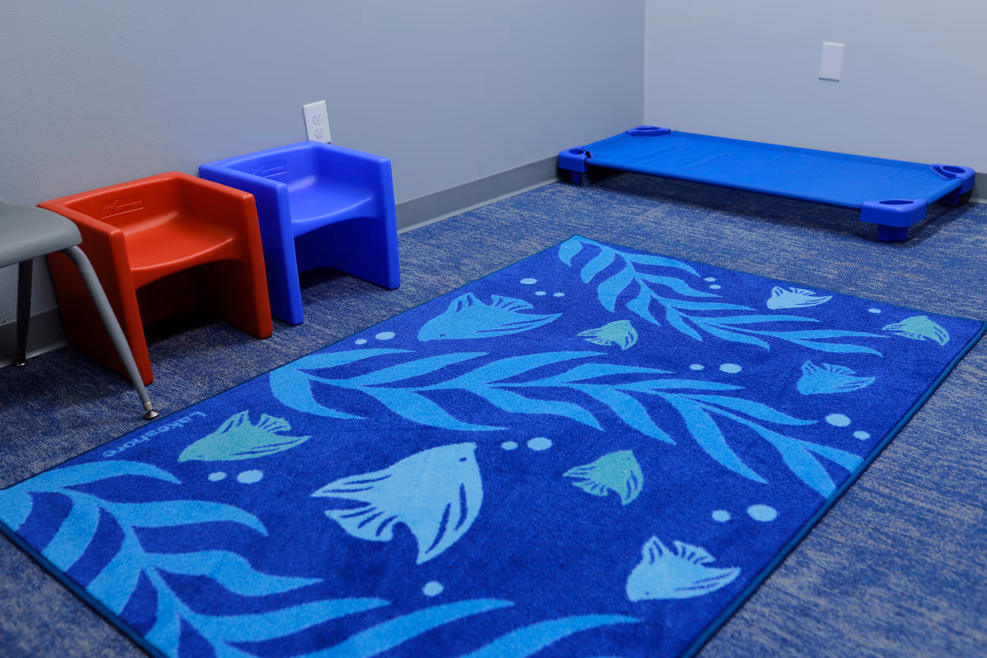 Colorful plastic chairs and a blue fish-pattern rug in a small therapy room.