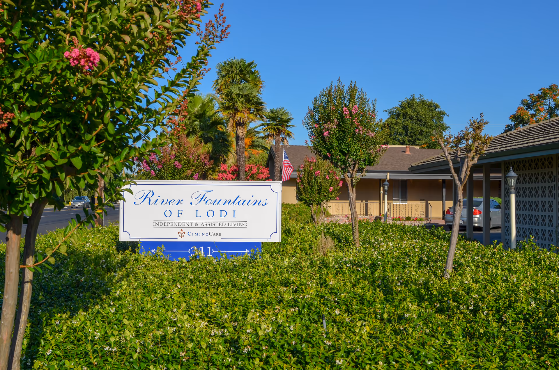 Exterior view of River Fountains of Lodi with sign, lush landscaping, and a driveway.