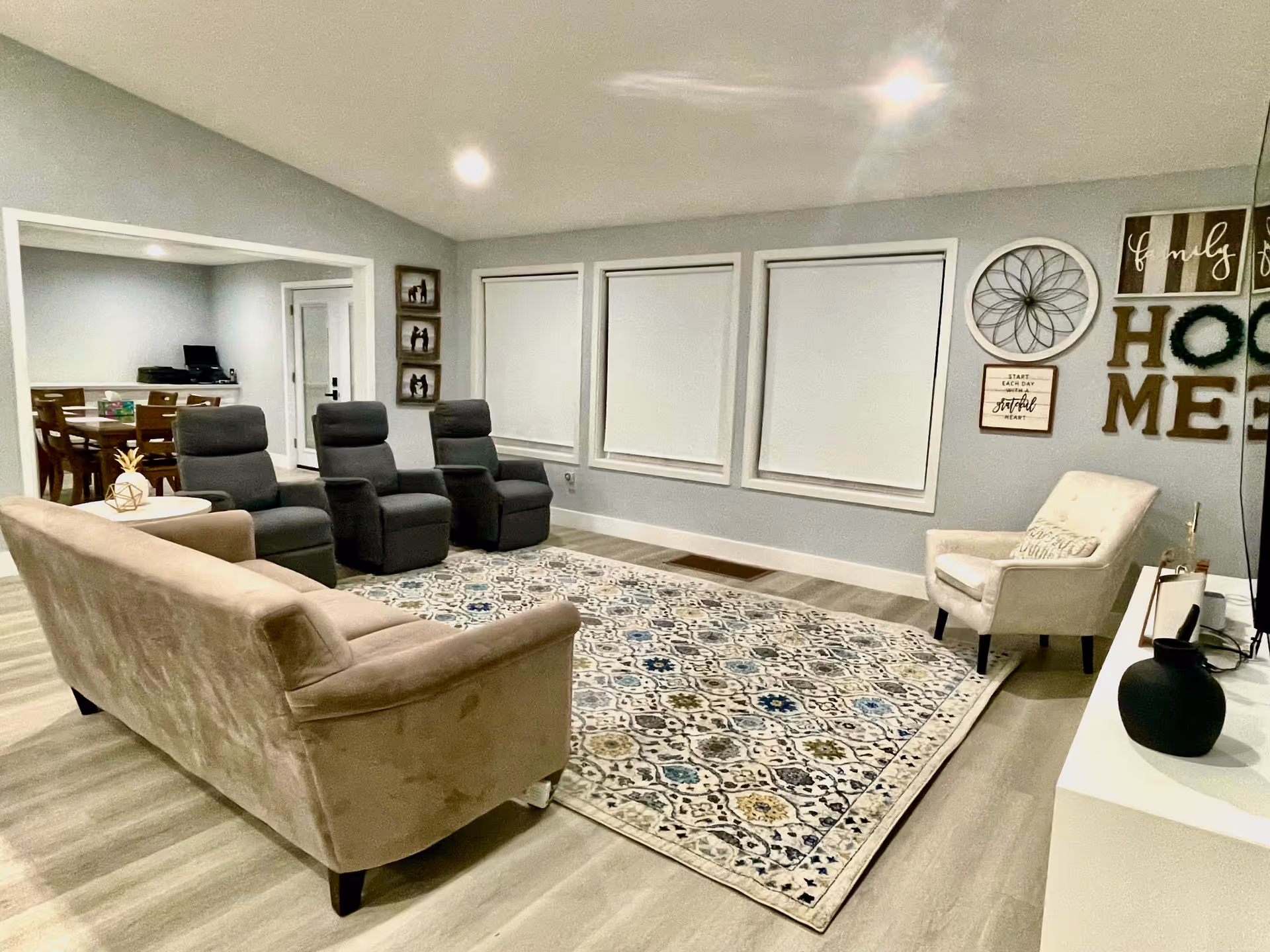 Cozy senior living lounge with beige sofa, recliners, rug, and decorative wall art.