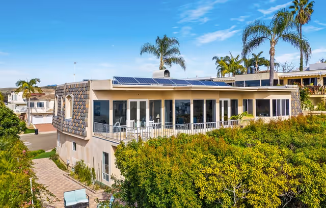 A modern beige senior living building with balcony, glass doors, solar panels, and palm trees.