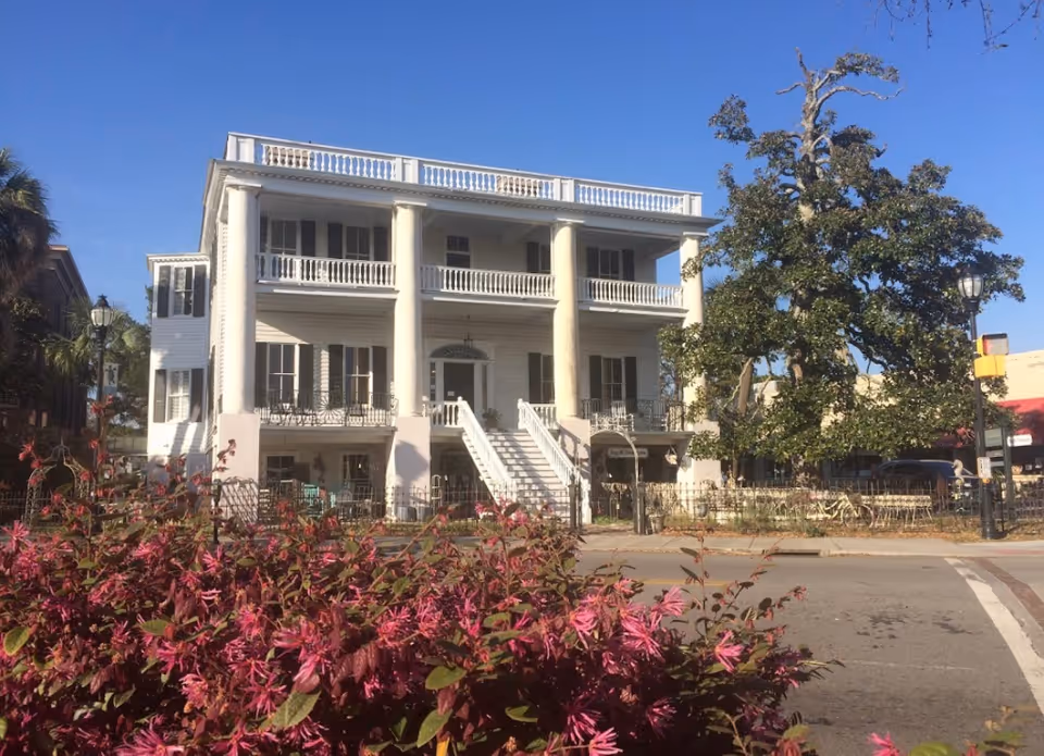 Omega Healthcare Services facility: white three-story building with columns, balconies, stairs, and pink flowers.