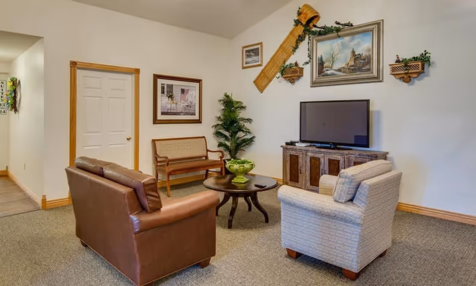 Cozy sitting area with a leather sofa, upholstered armchair, wooden bench, coffee table, TV on a cabinet and wall art.