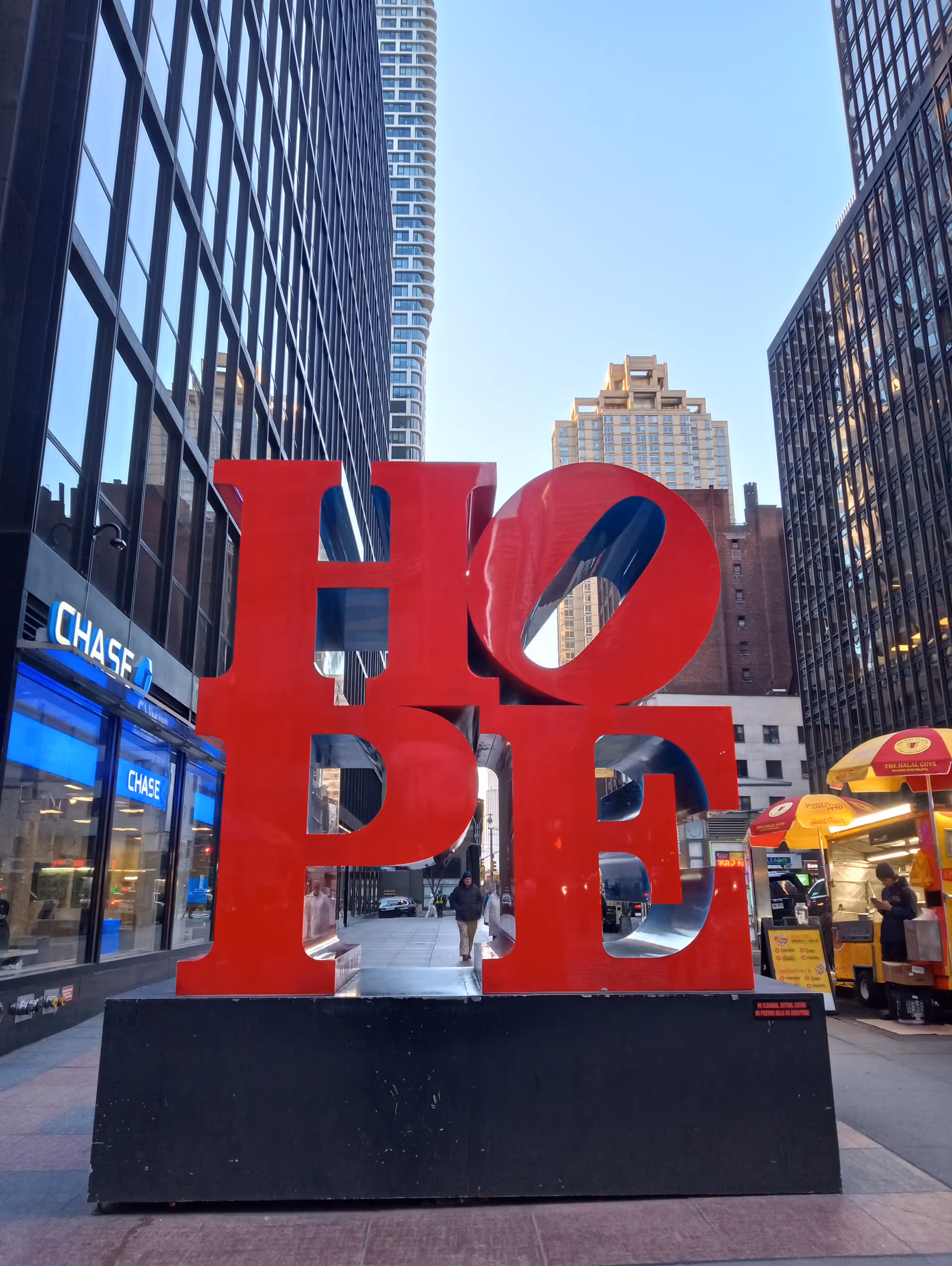 A large red HOPE sculpture stands in a city plaza.