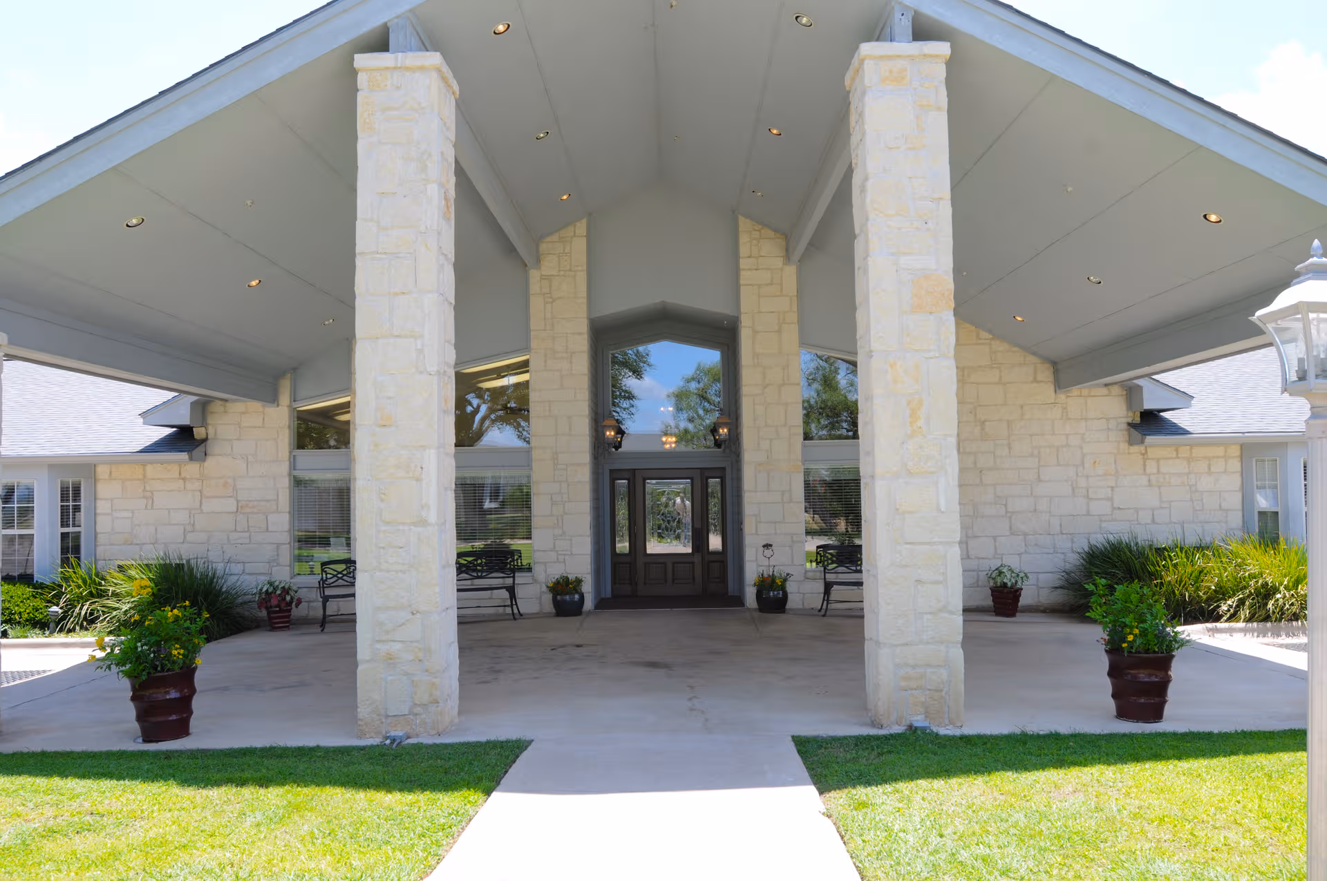 Stone-front entrance with tall columns, glass doors, and potted plants under a covered porte-cochere.