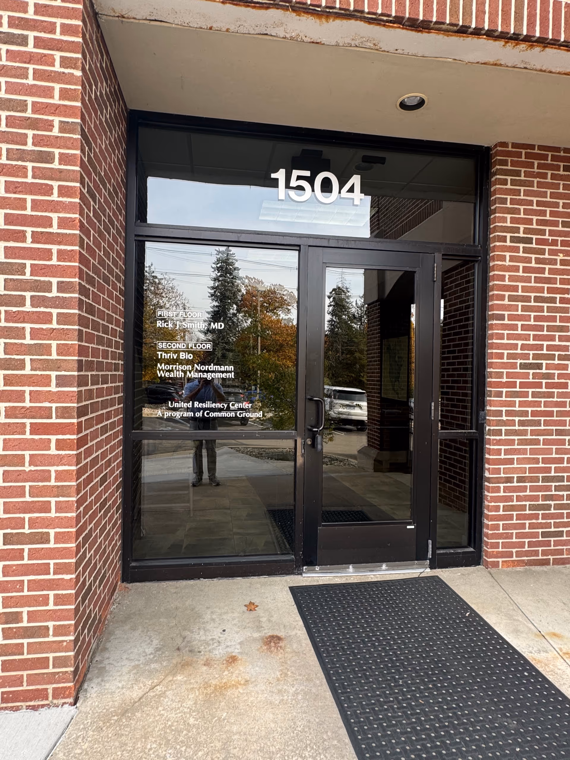 Brick building entrance with glass doors marked 1504 and a reflected street scene.