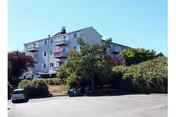 Front view of a three-story Canterbury Manor building with trees, shrubs, and a parked car.