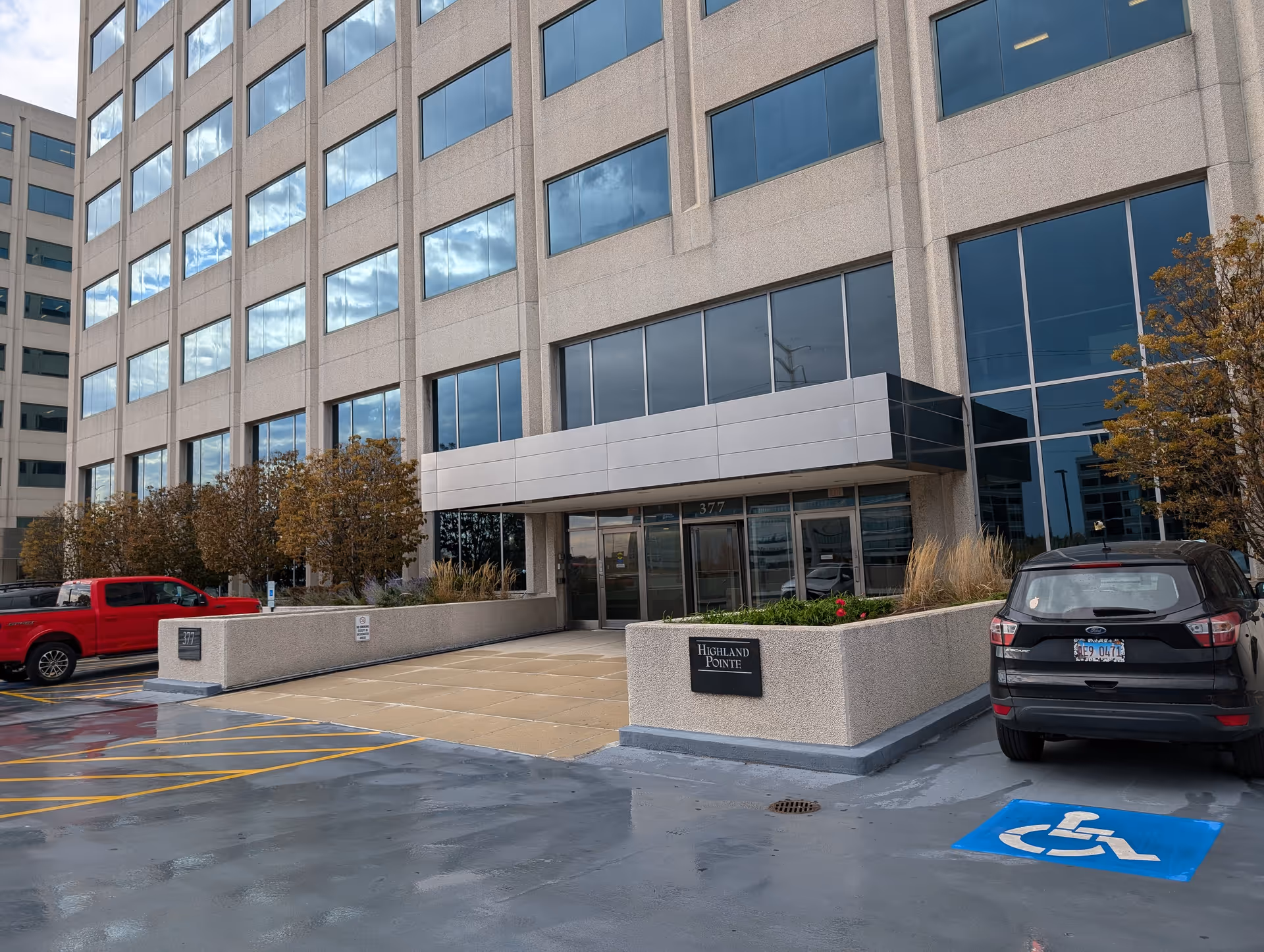 Front view of a tall beige office building with glass windows and a parking area.