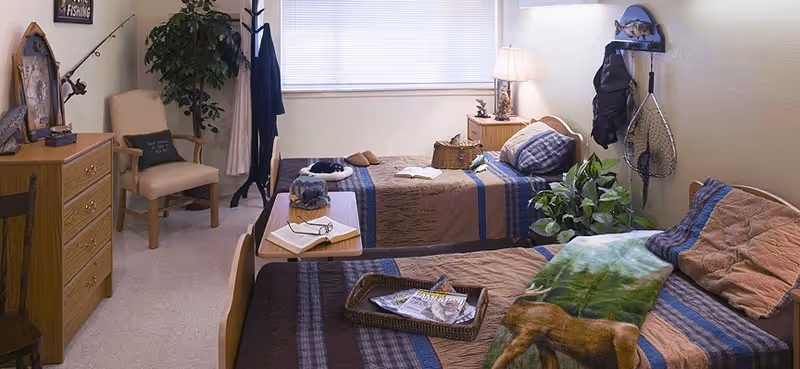 Two twin beds with striped quilts, a dresser, and plants in a resident bedroom.
