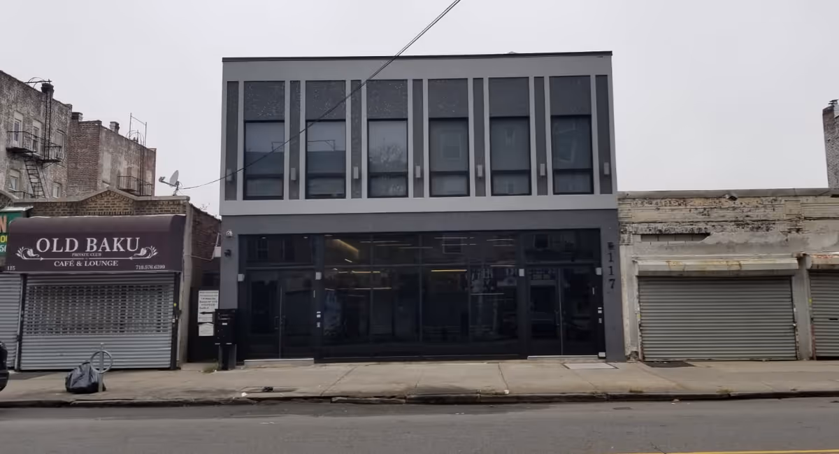 Urban street facade featuring a modern glass-front building between shuttered shops.