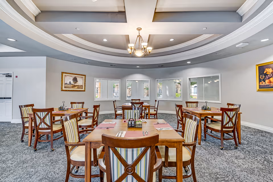 Bright dining room with wooden tables, chairs, chandeliers, and large windows.