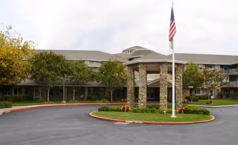 Exterior view of Creekside Oaks Retirement Community entrance with circular drive and flagpole.