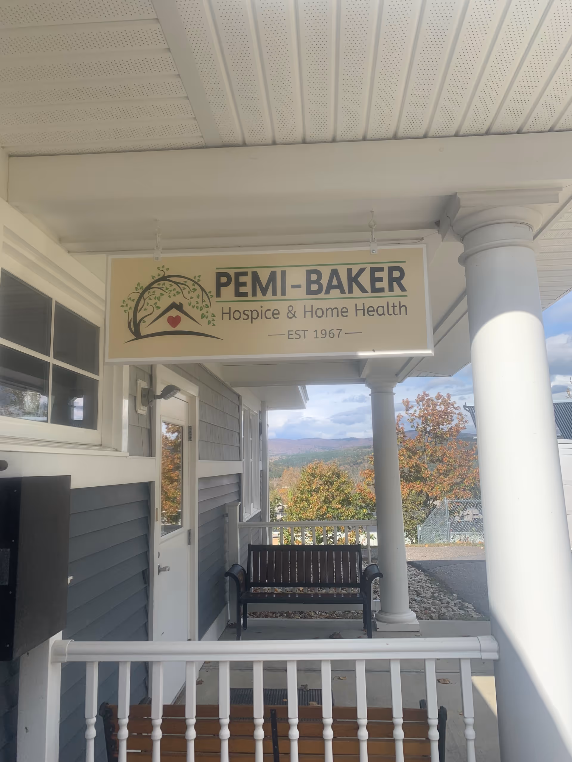 Front porch of Pemi-Baker Hospice and Home Health with bench and sign.