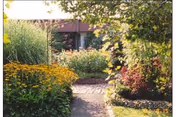 A garden path winds past yellow flowers toward a building entrance.