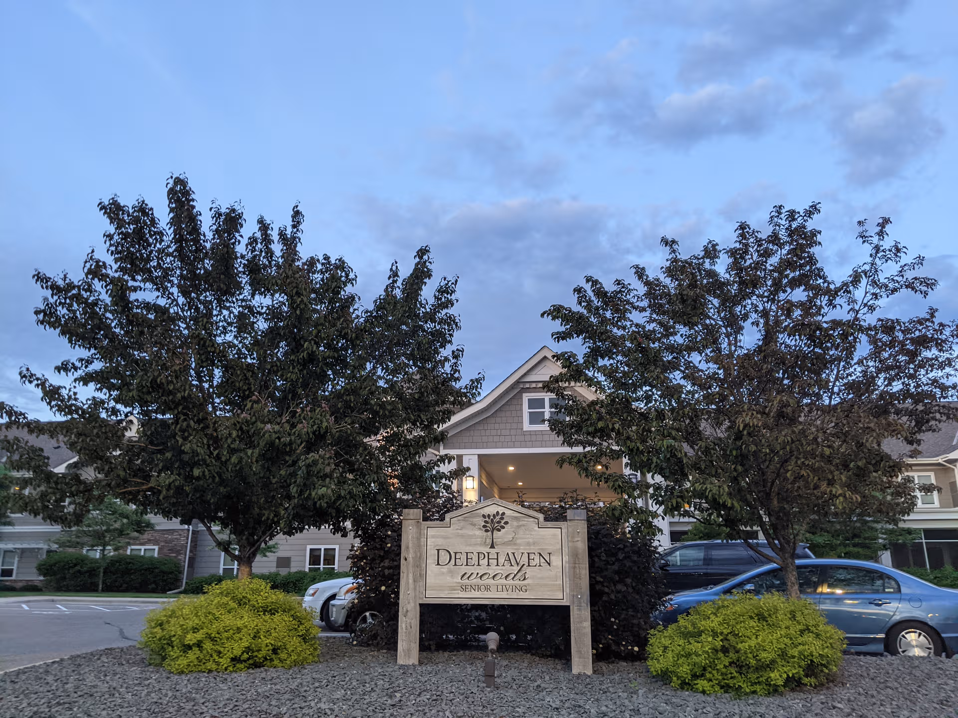 Exterior view of Deephaven Woods Senior Living entrance with trees and sign.