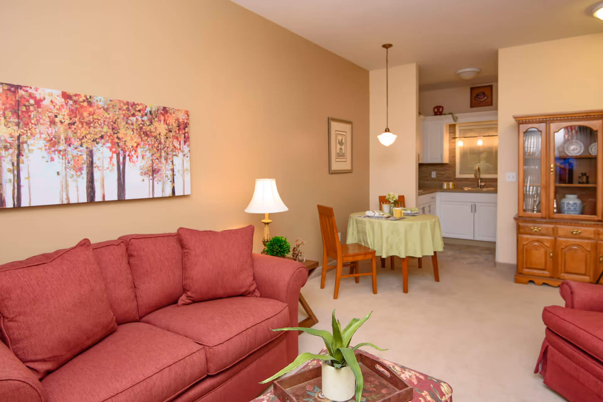 Cozy living room with a red sofa, small dining table, and an open kitchenette in the background.