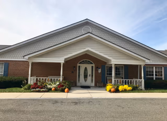 Arden Courts Annandale facility entrance with brick exterior, porch, and colorful autumn flowers