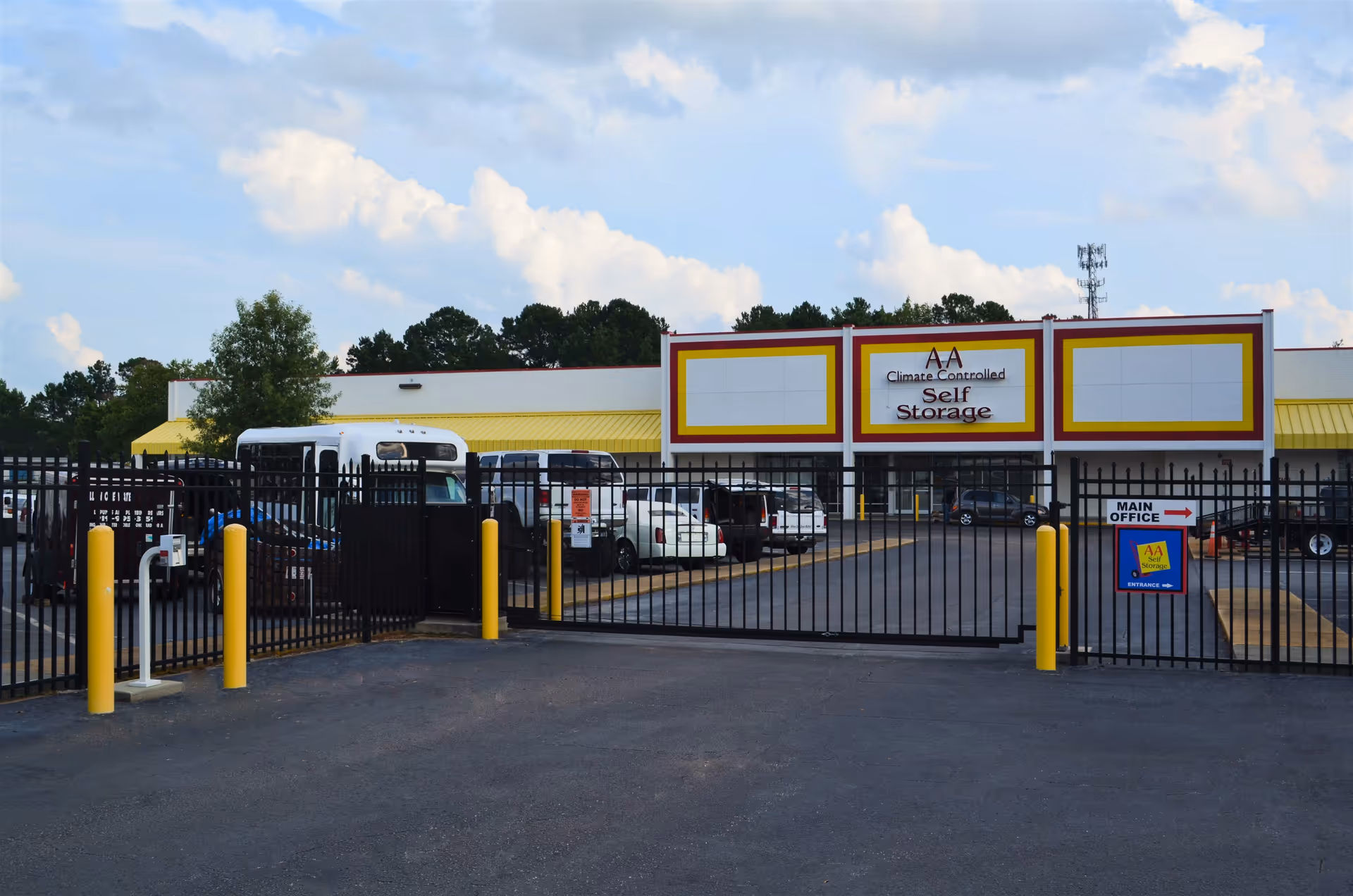 Gated entrance leads to a climate-controlled self-storage facility with a yellow-trimmed front.