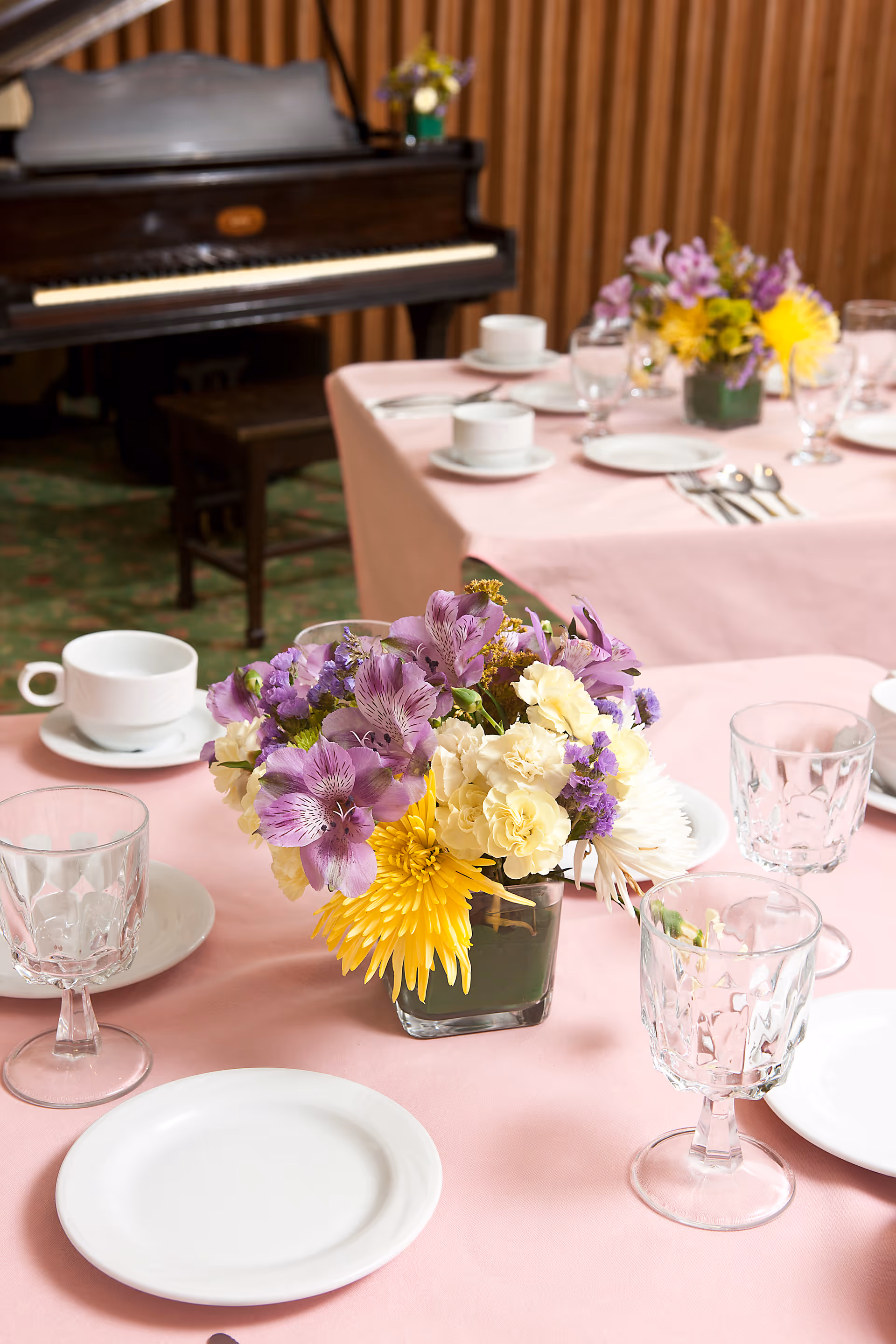Pink tablecloths with floral centerpieces and glassware in a dining room.