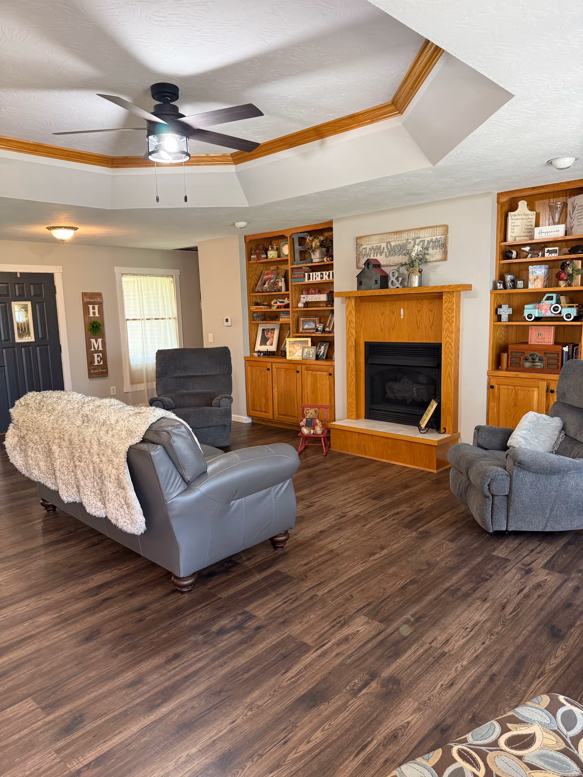 Cozy living room with fireplace, wooden shelves, ceiling fan, and reclining chairs.