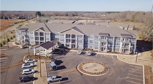 A multi-story senior living facility exterior with a circular driveway and surrounding parking lot.